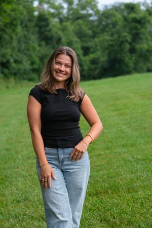 Woman in casual outfit smiling and posing on a sunny grassy slope.