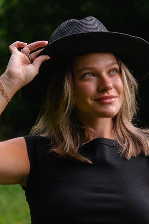 Portrait session featuring playful poses with a black hat in natural lighting.