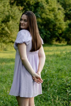 Woman in light summer dress posing naturally in green field.