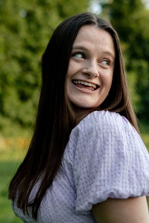 A person in a white textured top poses playfully against a green outdoor background.