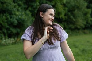 Someone wearing a lilac dress smiles while posing in a natural outdoor setting.