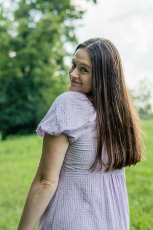 A person wearing a textured white dress poses against a natural green backdrop.