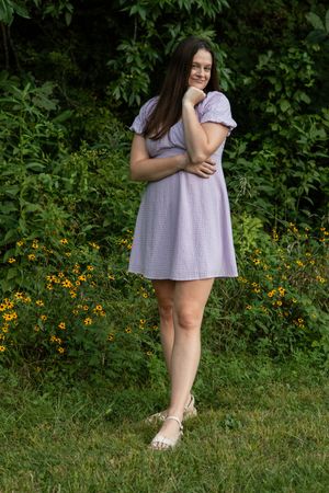 A figure in a casual dress stands among wildflowers and grass on a summer day.