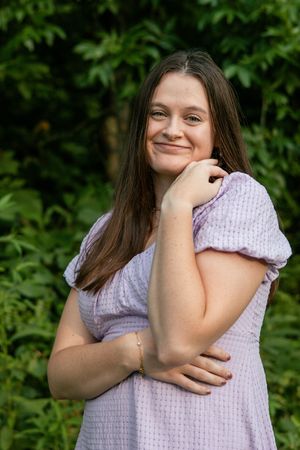Someone in a textured dress makes expressive poses against a leafy green background.