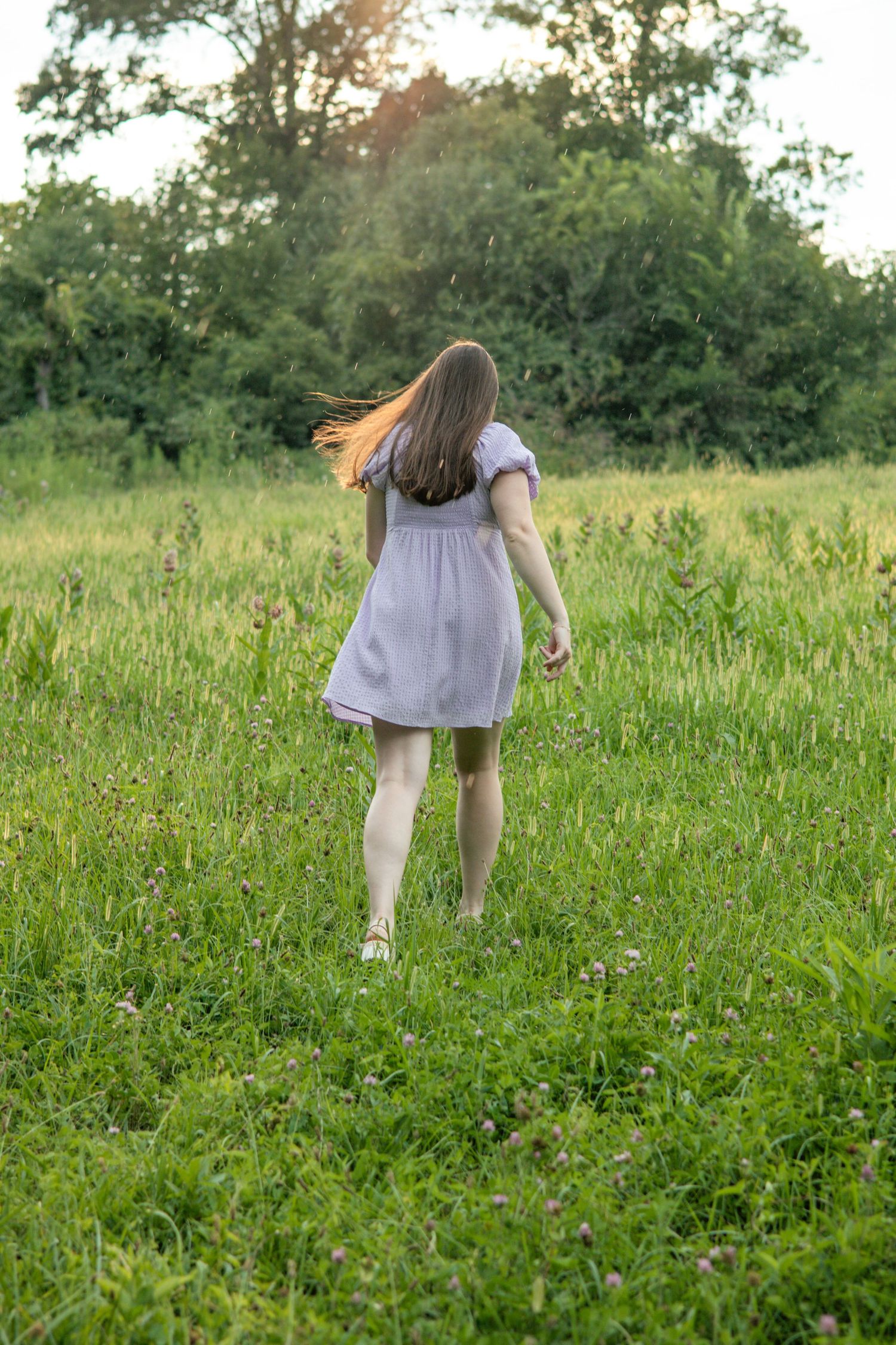 Woman in white dress twirling playfully in a green summer meadow.