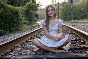 Figure in white floral dress sits gracefully on vintage railroad tracks during golden hour.