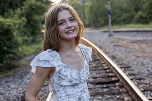 Figure in white dress stands on railroad tracks during sunset photo session.
