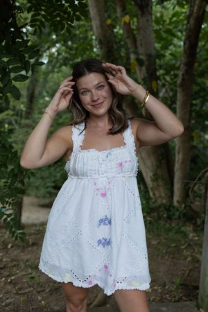 Person in white eyelet top with colorful accents poses playfully against forest backdrop.