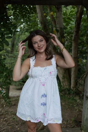 White summer dress with delicate floral details photographed against a natural forest backdrop.