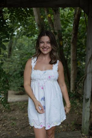 Casual outdoor portrait session featuring a white sleeveless dress with pink and blue embroidered accents.