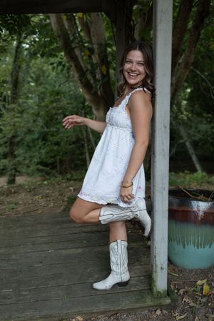 Outdoor fashion shoot featuring white cowboy boots and eyelet dress against wooden pillars.