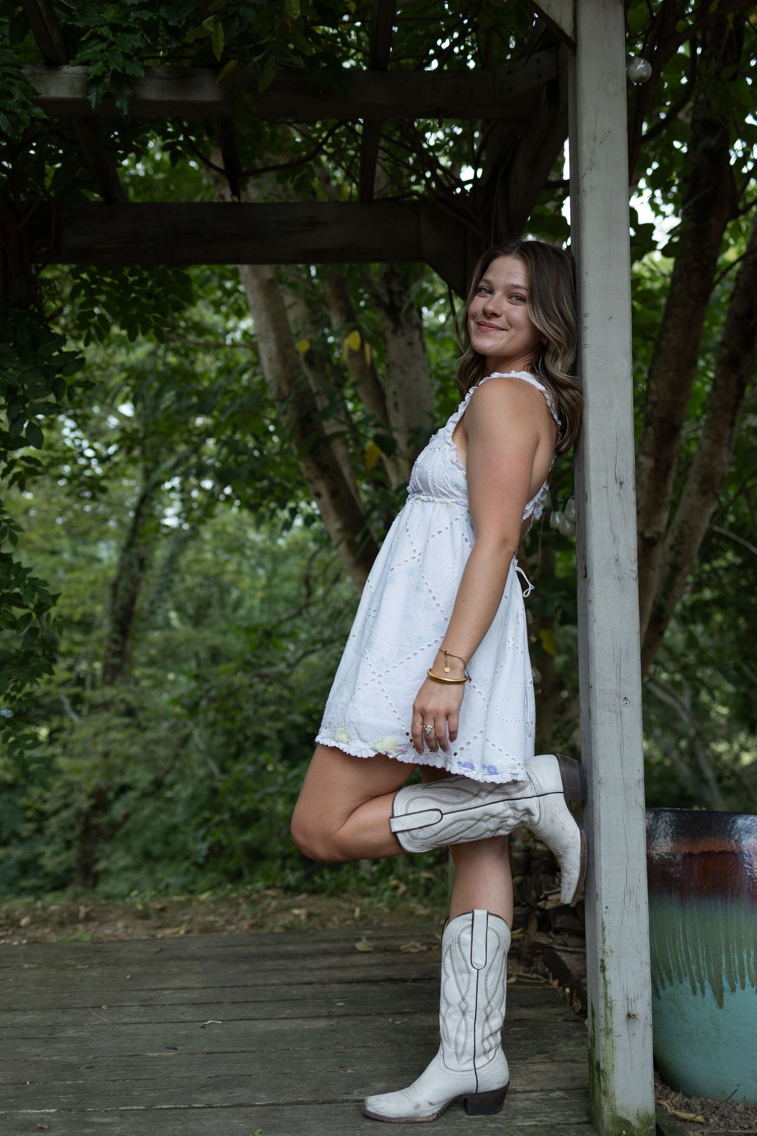 Rustic outdoor photoshoot showcasing western boots and white eyelet dress.
