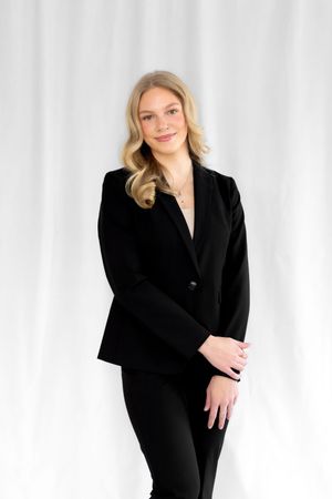 Professional studio portrait of someone in a black blazer and blonde hair against a white backdrop.