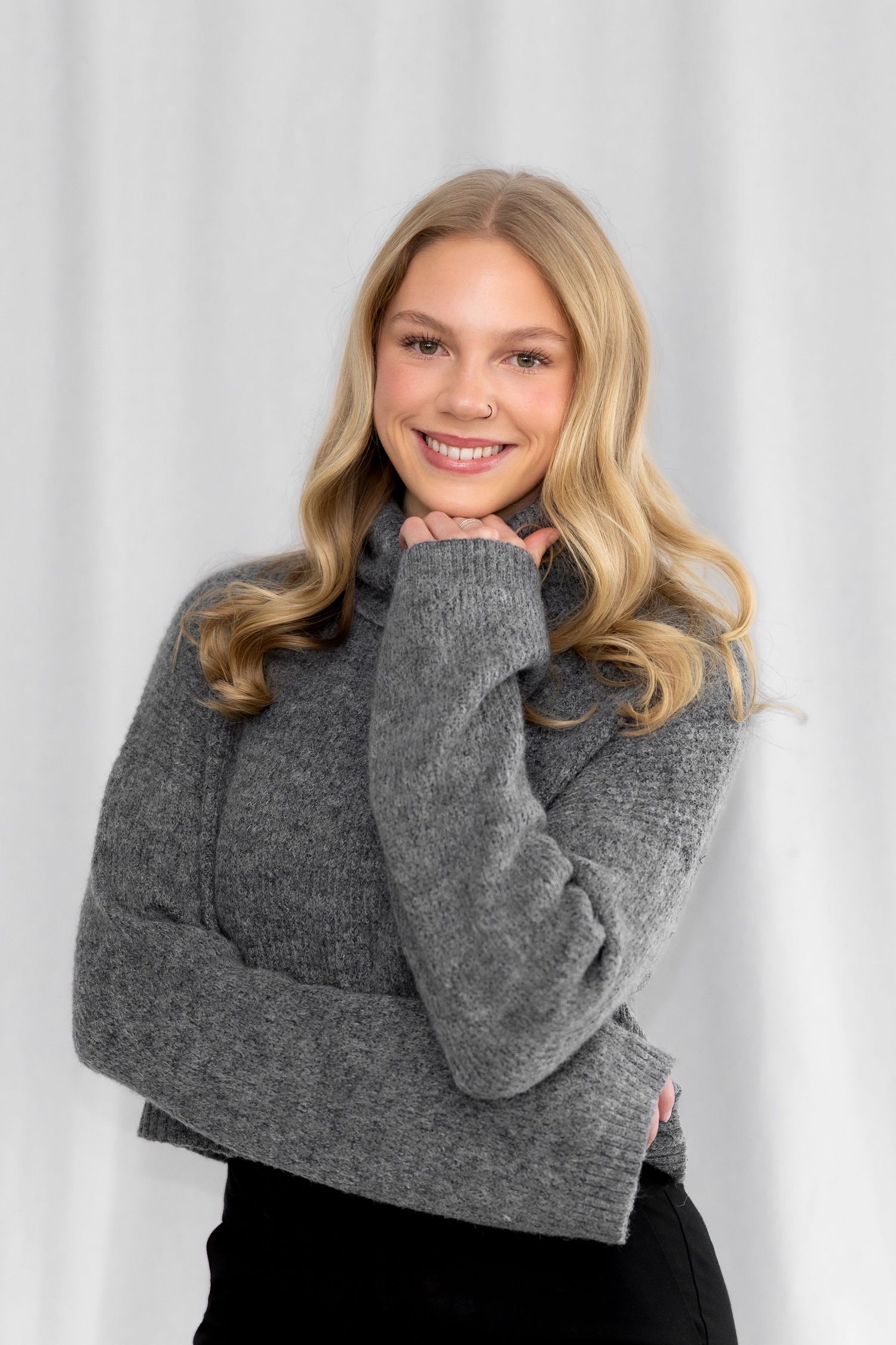 A person wearing a cozy gray knit sweater poses playfully against a white background in a photo series.
