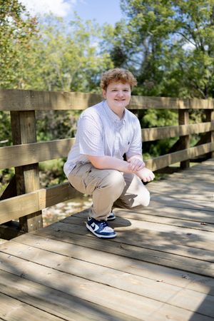 Child crouches on wooden bridge deck wearing casual summer attire.
