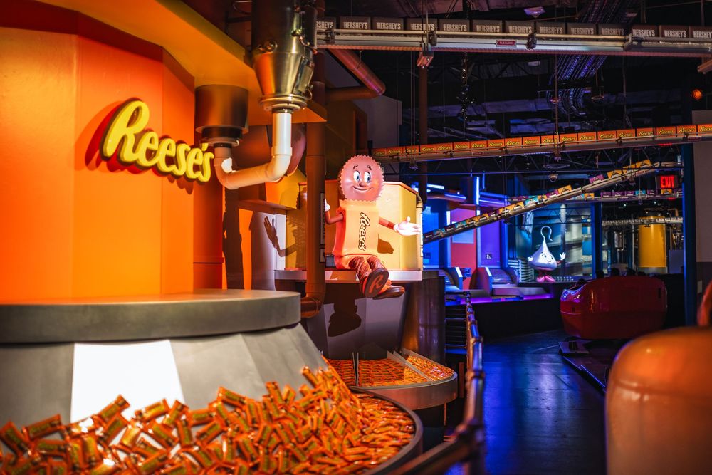 Large bowl of Reese's candy pieces displayed in an orange-themed storefront interior with neon lighting.