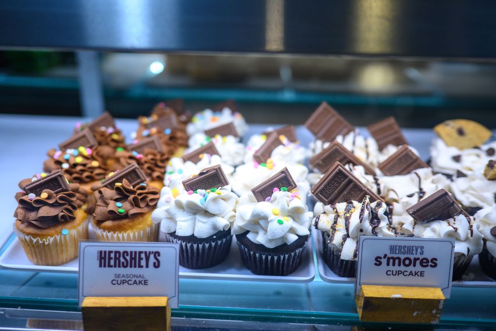 Display of gourmet cupcakes including Hershey's chocolate and s'mores flavors in a bakery case.