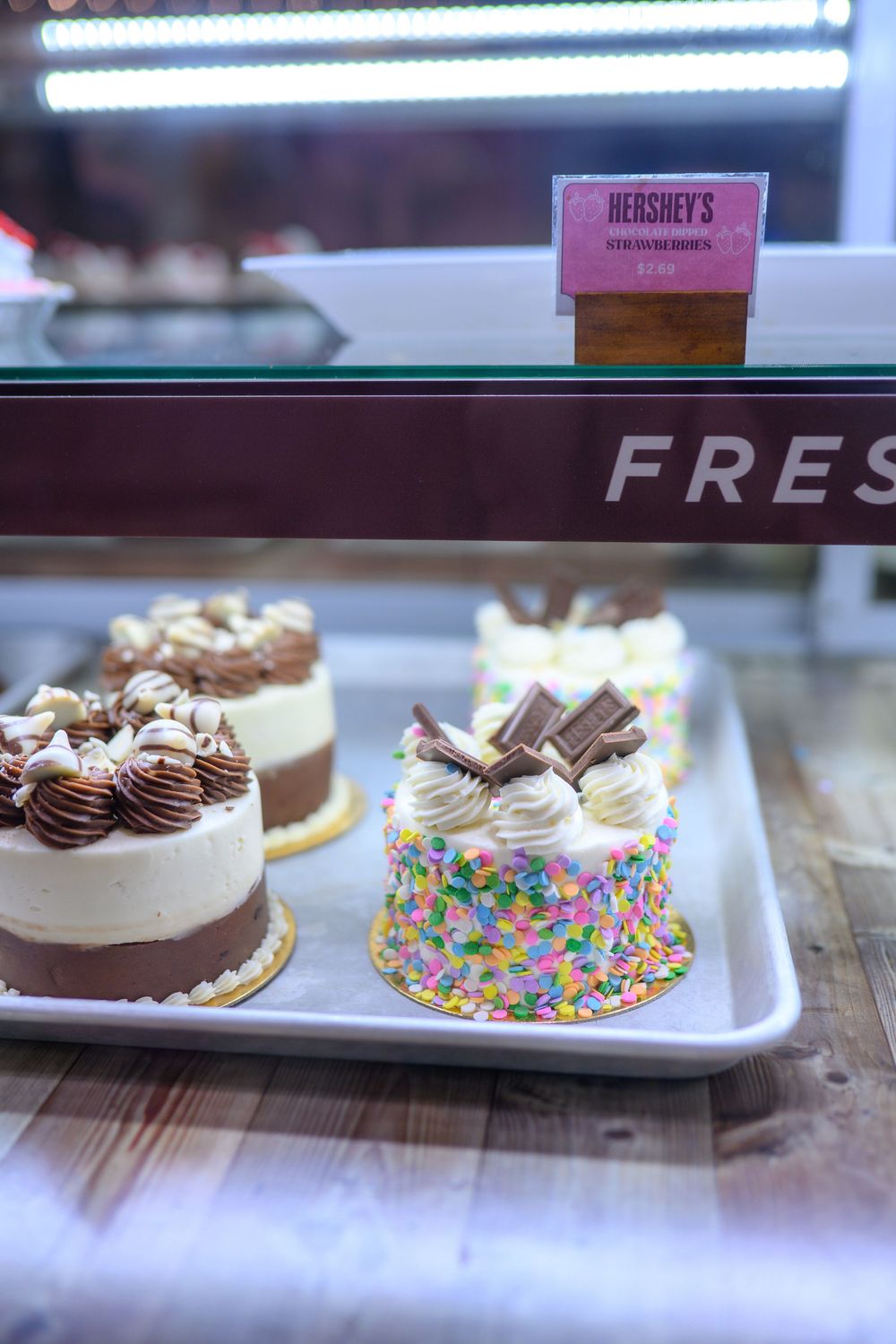Five delicious chocolate cakes topped with decorative frosting and candies displayed on a bakery counter.