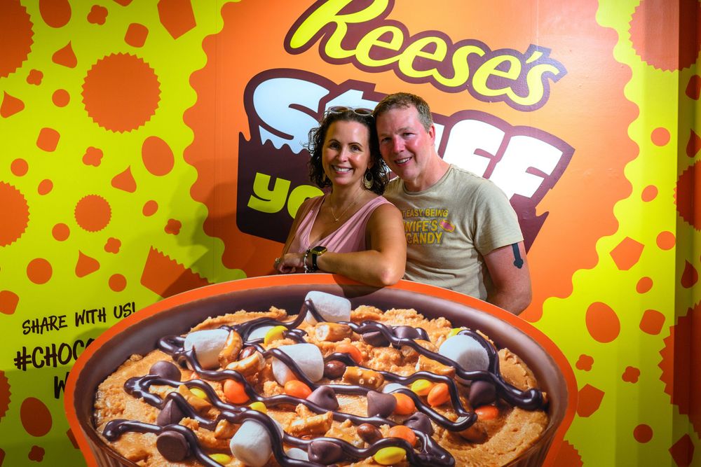 A large bowl of Reese's Puffs cereal displayed against a bright orange and green background with Reese's branding.