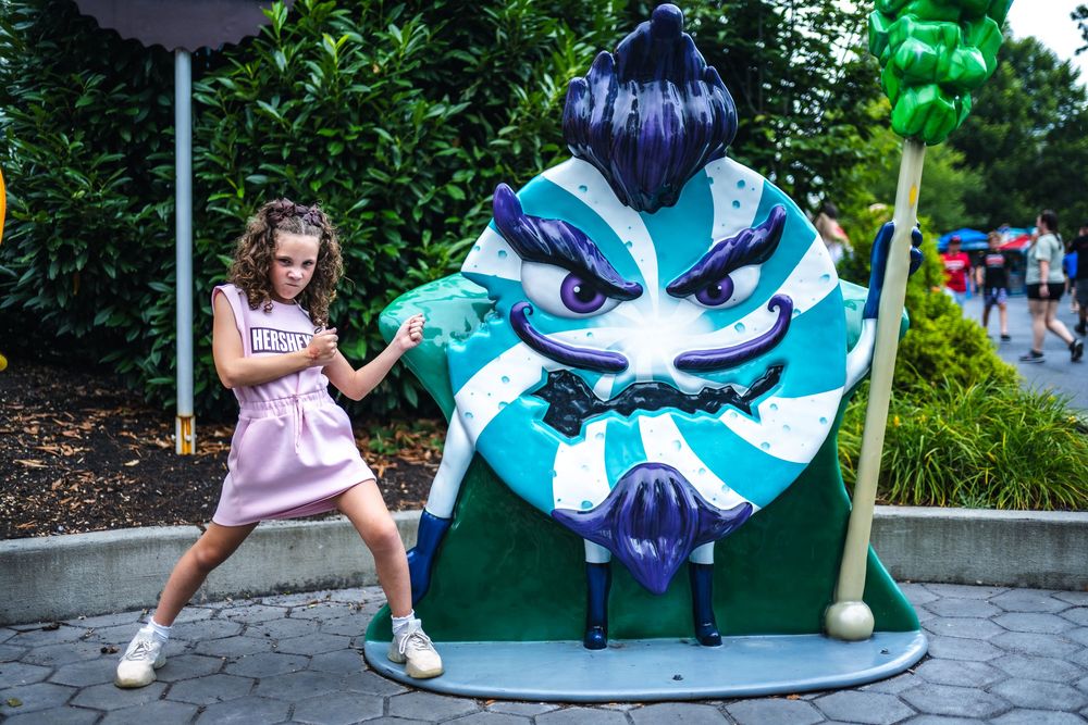 A playful scene at a theme park featuring someone posing next to a large blue and white animated character display.