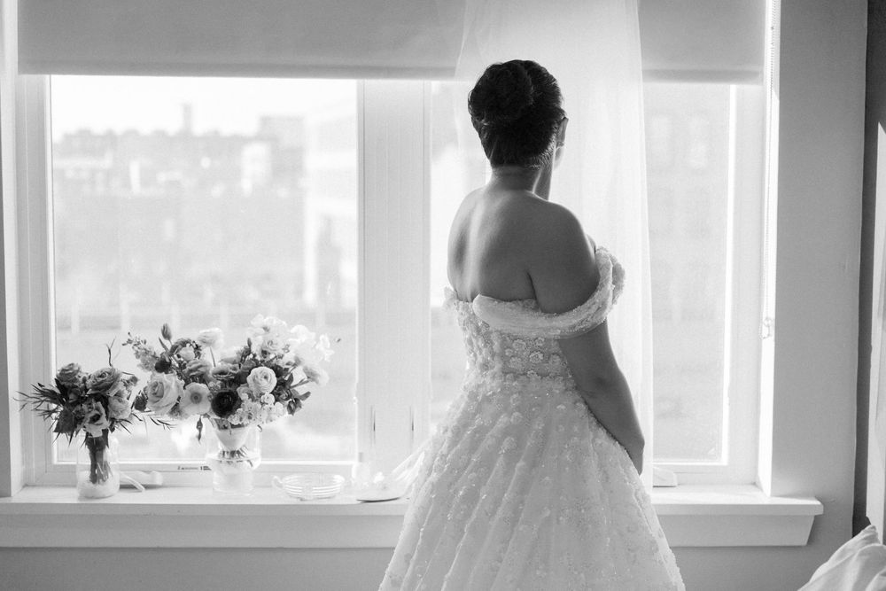 Silhouette of bride in wedding dress looking out window with flowers on windowsill.