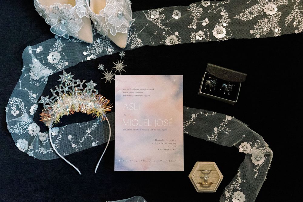 Delicate white lace and floral details arranged on a dark background with wedding stationery.