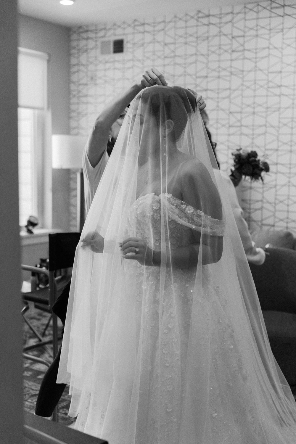 Black and white photo of bride having veil adjusted in preparation room.