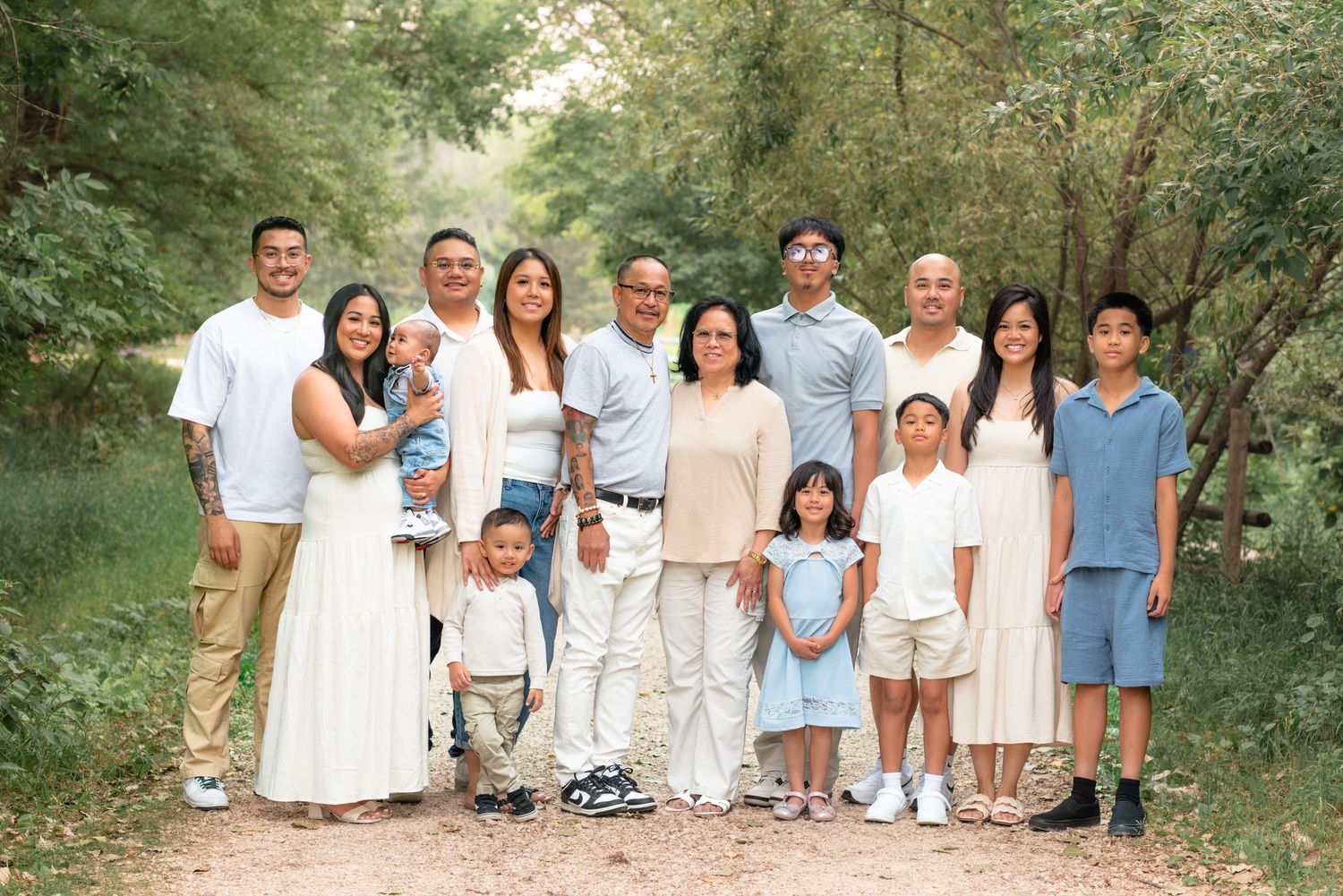 A family of four sits together outdoors for a casual portrait photo during a sunny day.