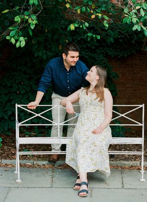 A couple shares a candid moment while sitting on a decorative white metal bench outdoors.