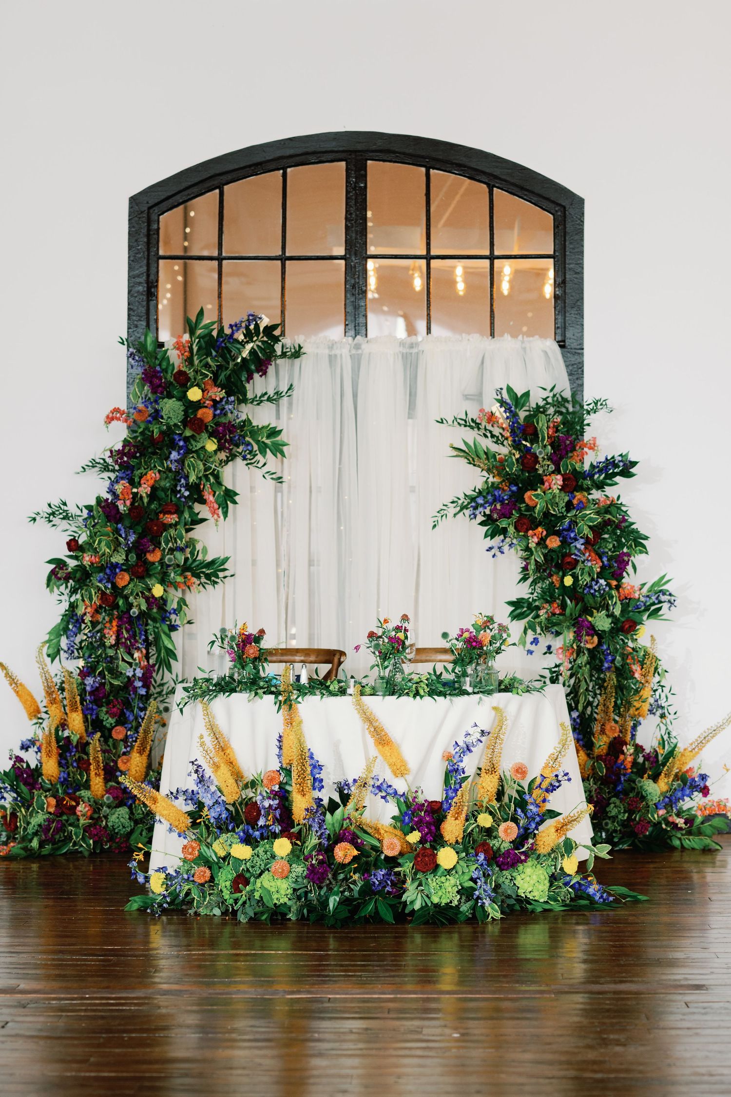 Wedding ceremony backdrop with cascading floral arrangements and golden accents against a white fabric wall.