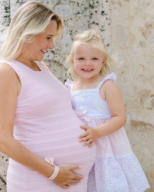 Two figures in white and pink outfits sharing a tender moment against a stone wall.