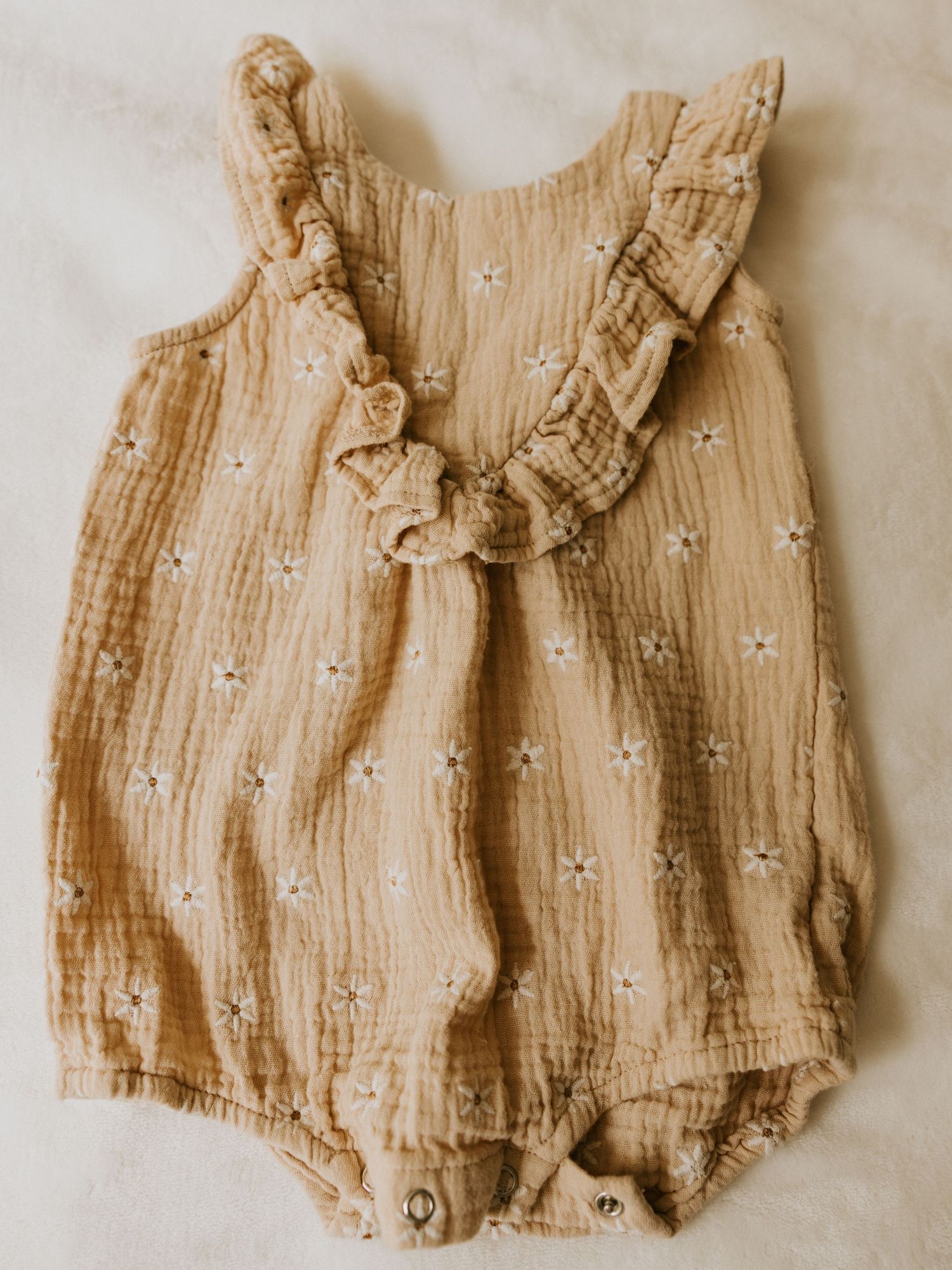 Formal infant outfit with beige vest, white shirt, light blue bow tie, and matching shorts hanging on wooden ladder shelf.