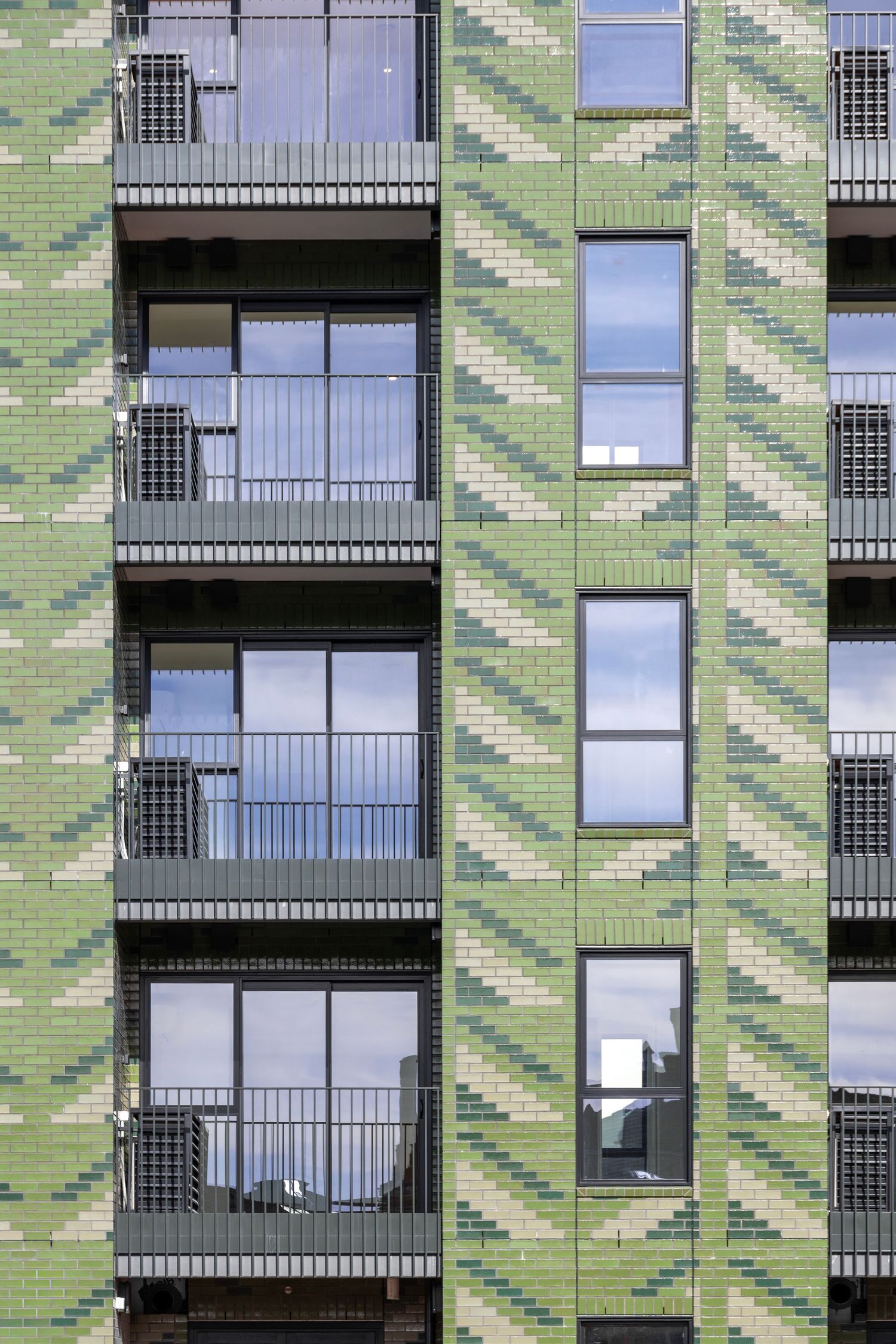 Apartment building with green tile-like cladding and rhythmic window arrangement.