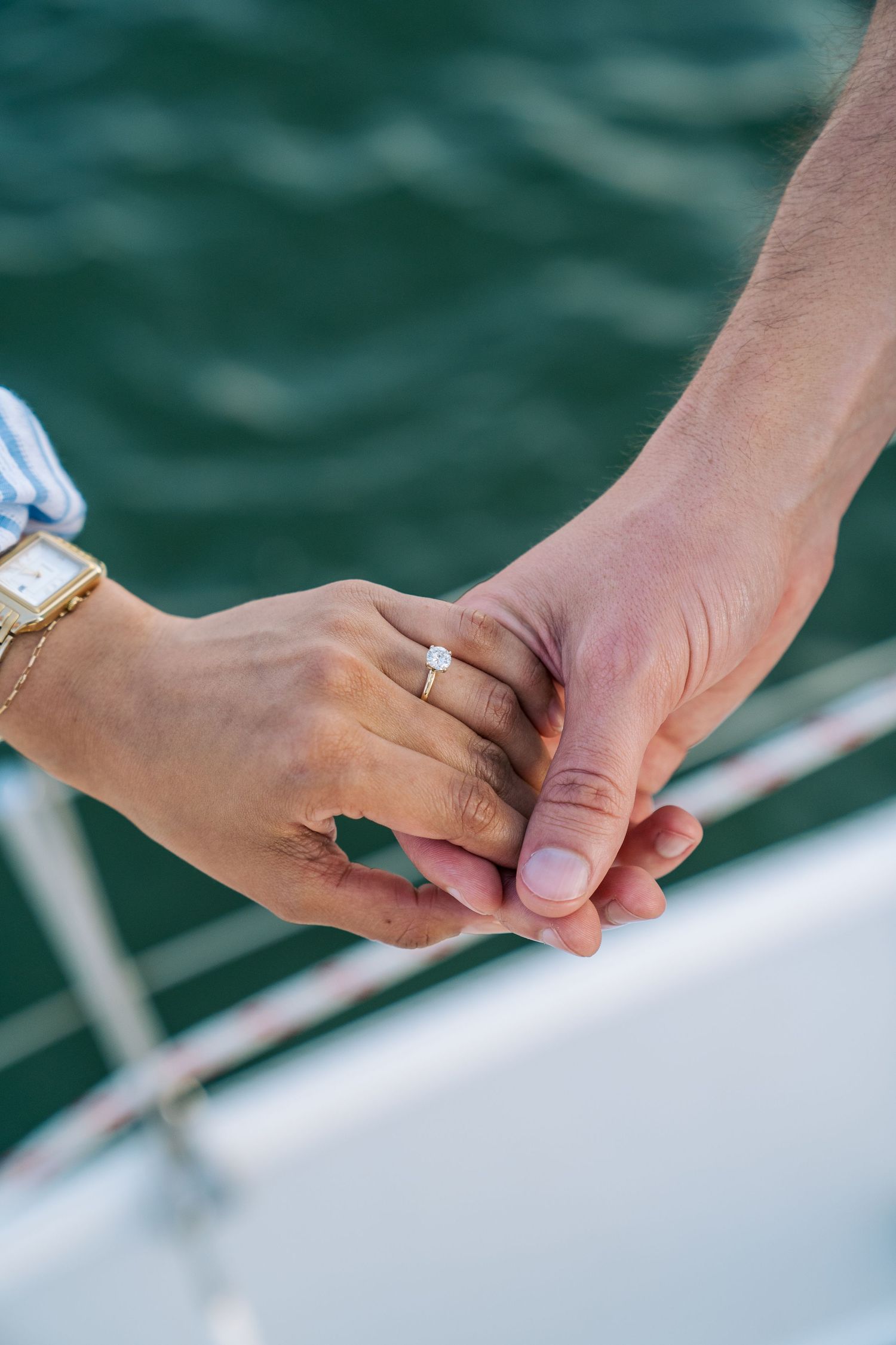 Close-up view of two hands holding each other against a serene turquoise water background.