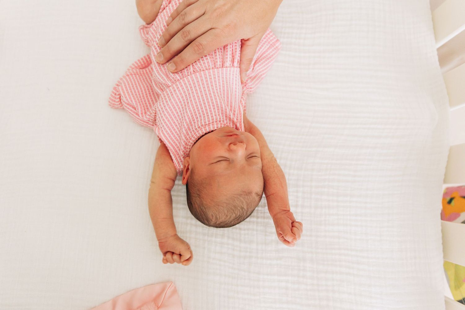 A sleeping baby in pink striped clothing lies peacefully on white bedding.