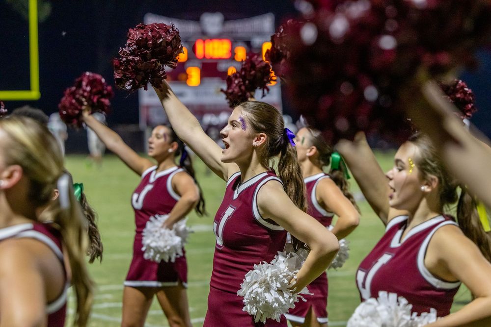 College cheerleaders in maroon uniforms perform synchronized dance routine during sporting event.