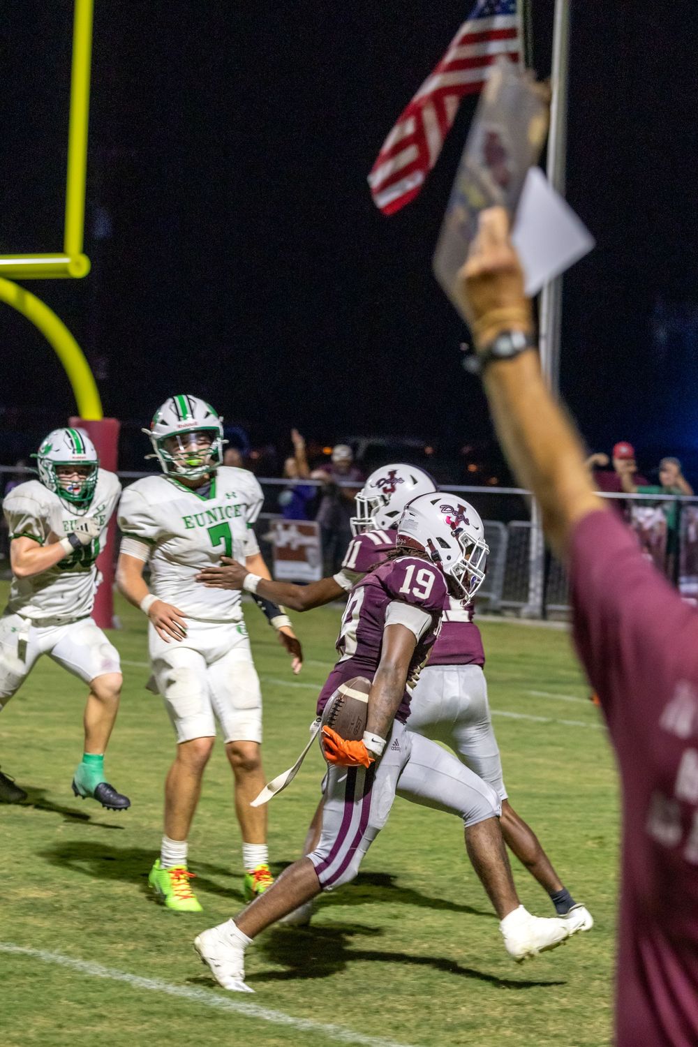 Football players in white and maroon uniforms compete during a nighttime game under stadium lights.