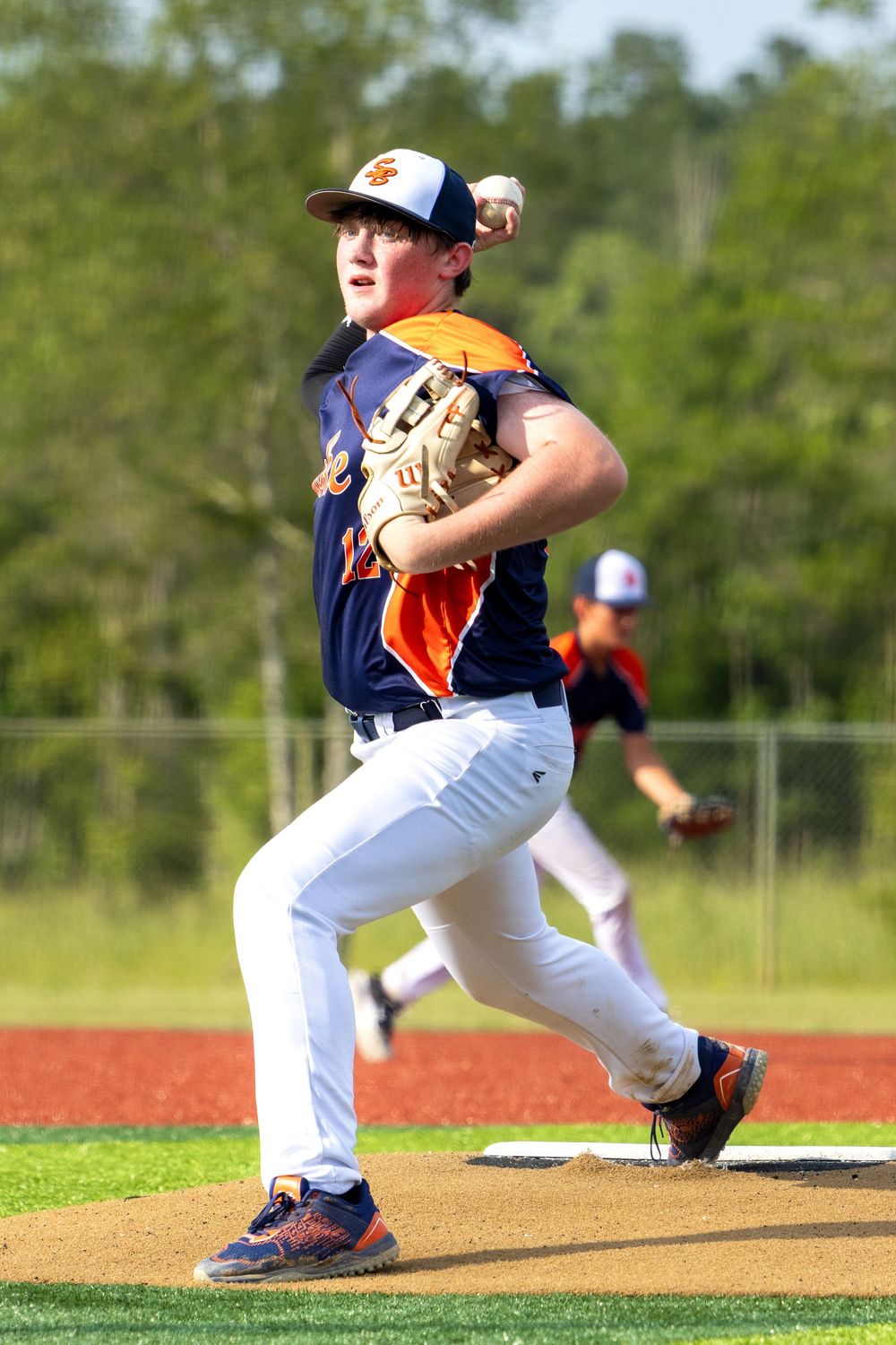 Baseball player in navy and orange uniform demonstrates pitching sequence on pitcher's mound.