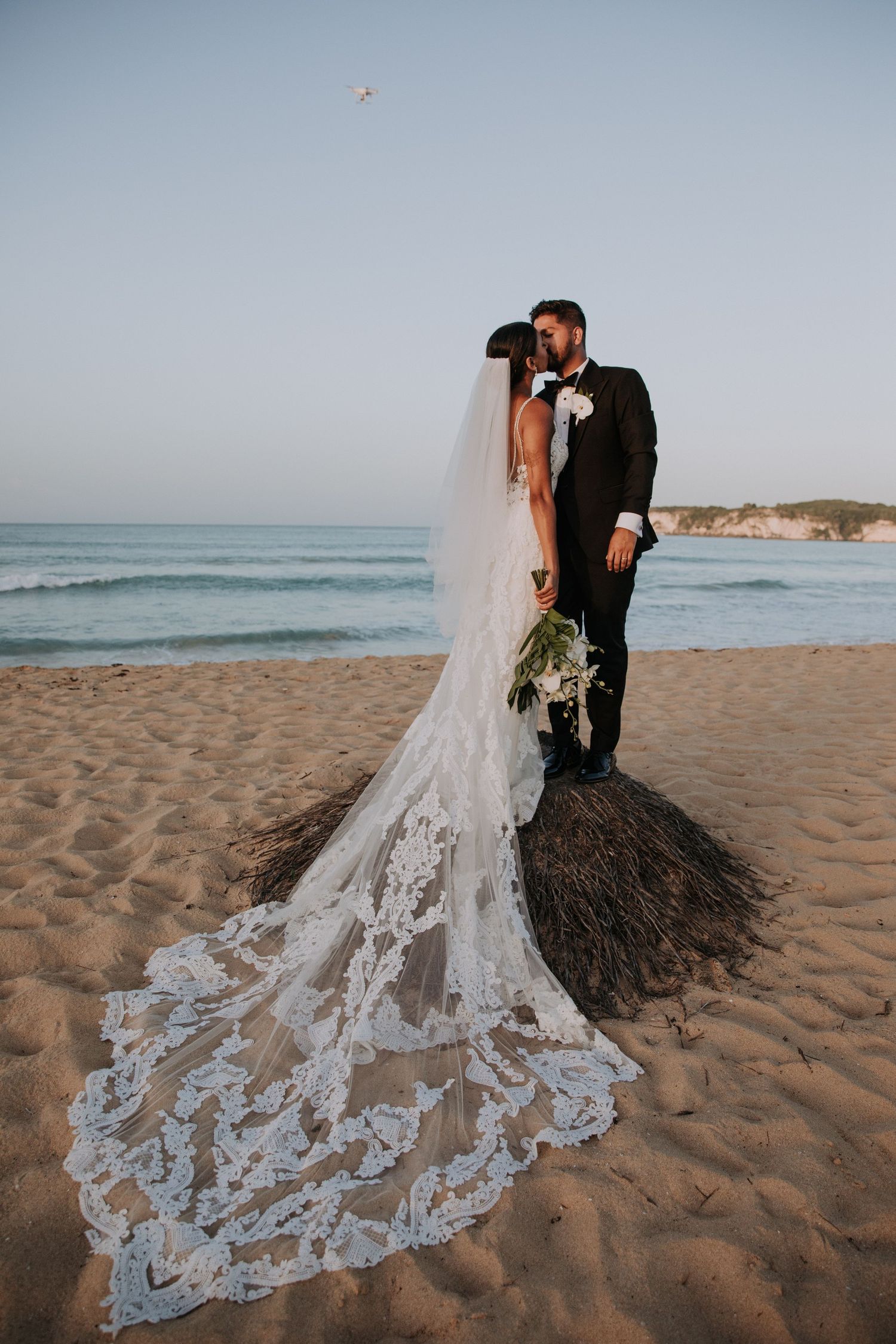 A romantic beach wedding photoshoot featuring a stunning lace train dress against coastal backdrop.
