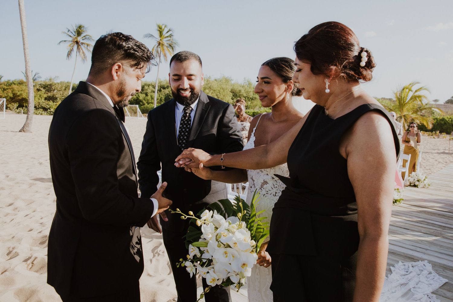 A wedding ceremony taking place at a beachside venue with guests standing in formal attire.