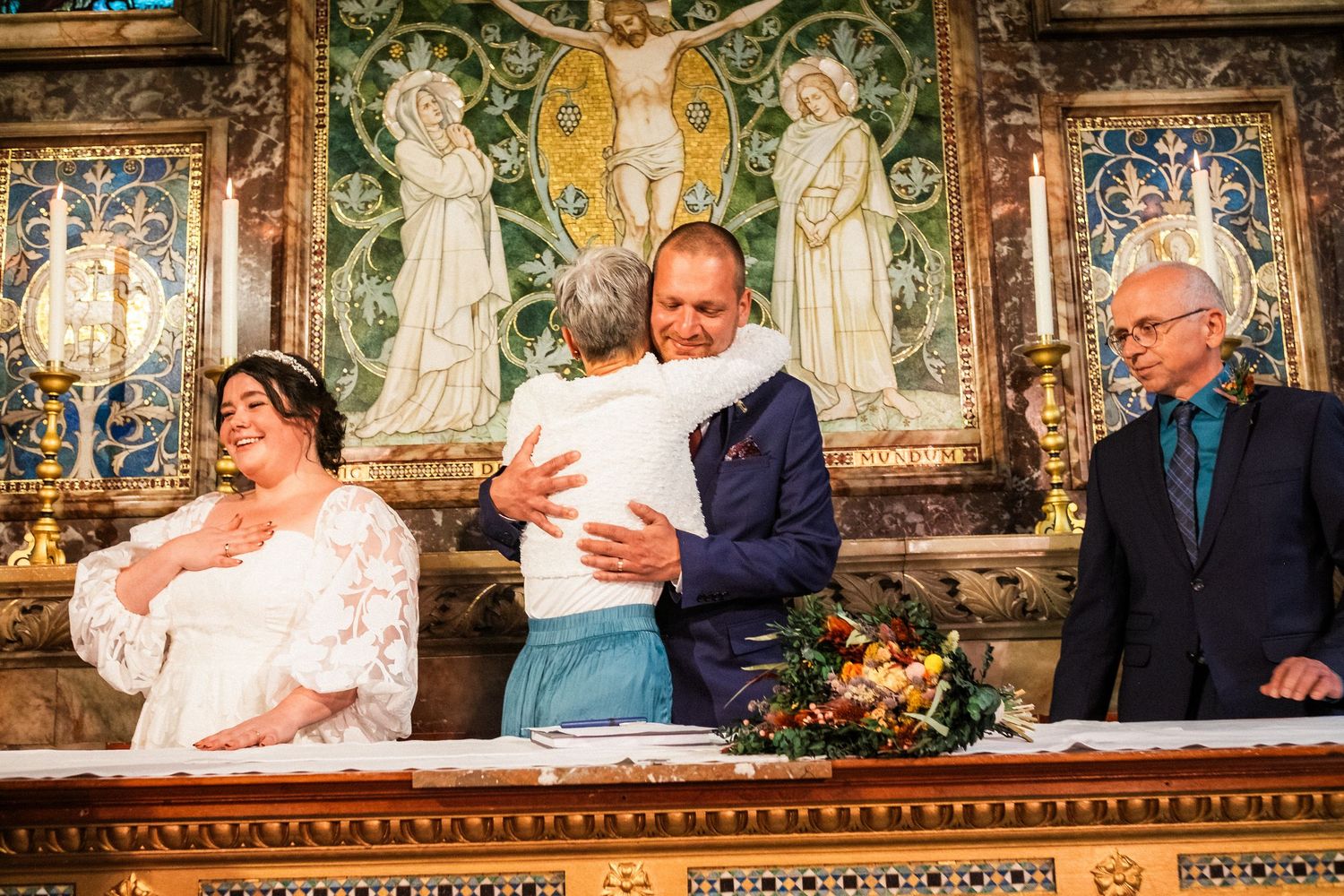 A baptism ceremony takes place at an ornate church altar with decorative mosaic artwork and religious imagery in the background.