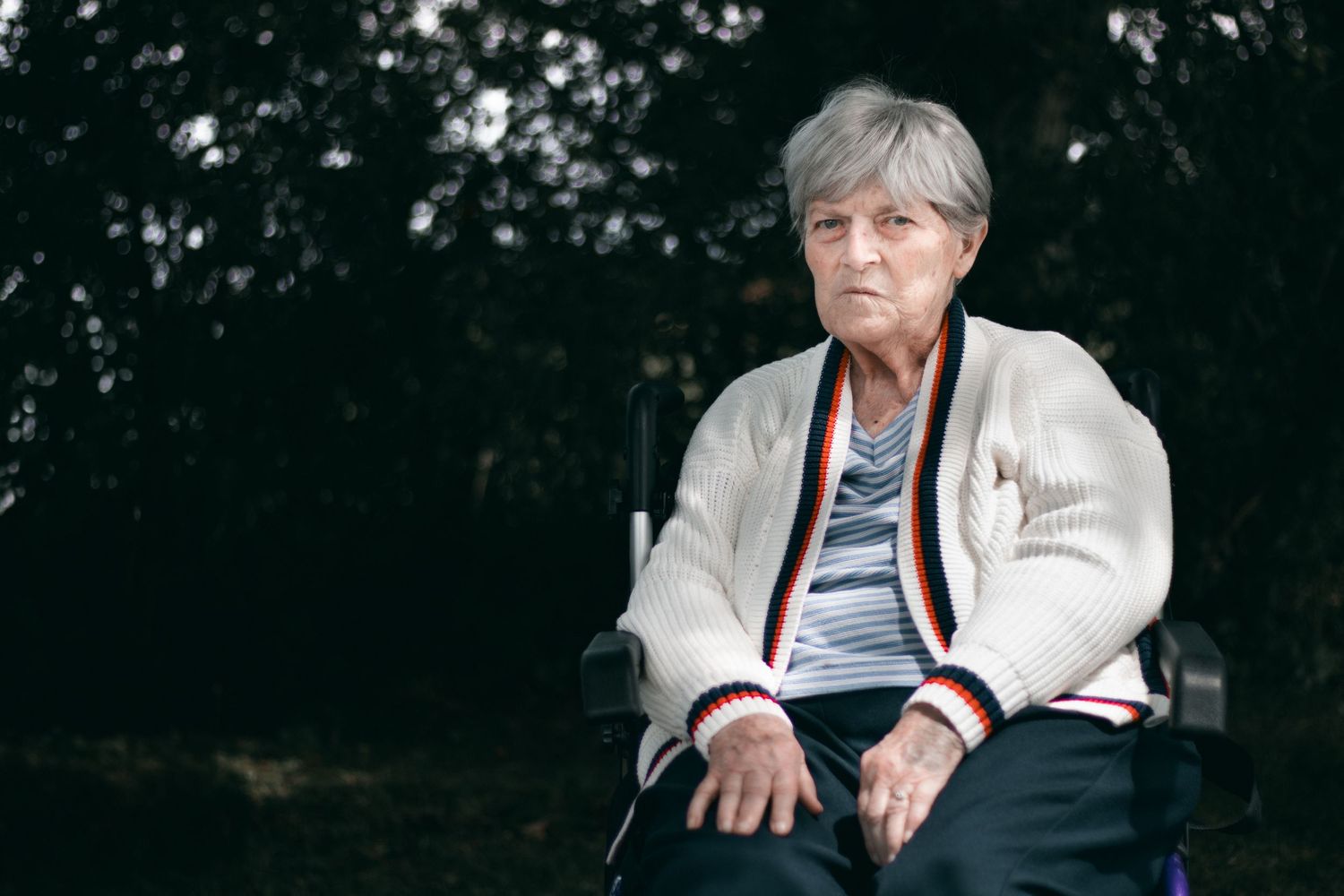 Person wearing a white cardigan seated outdoors making hand gestures.
