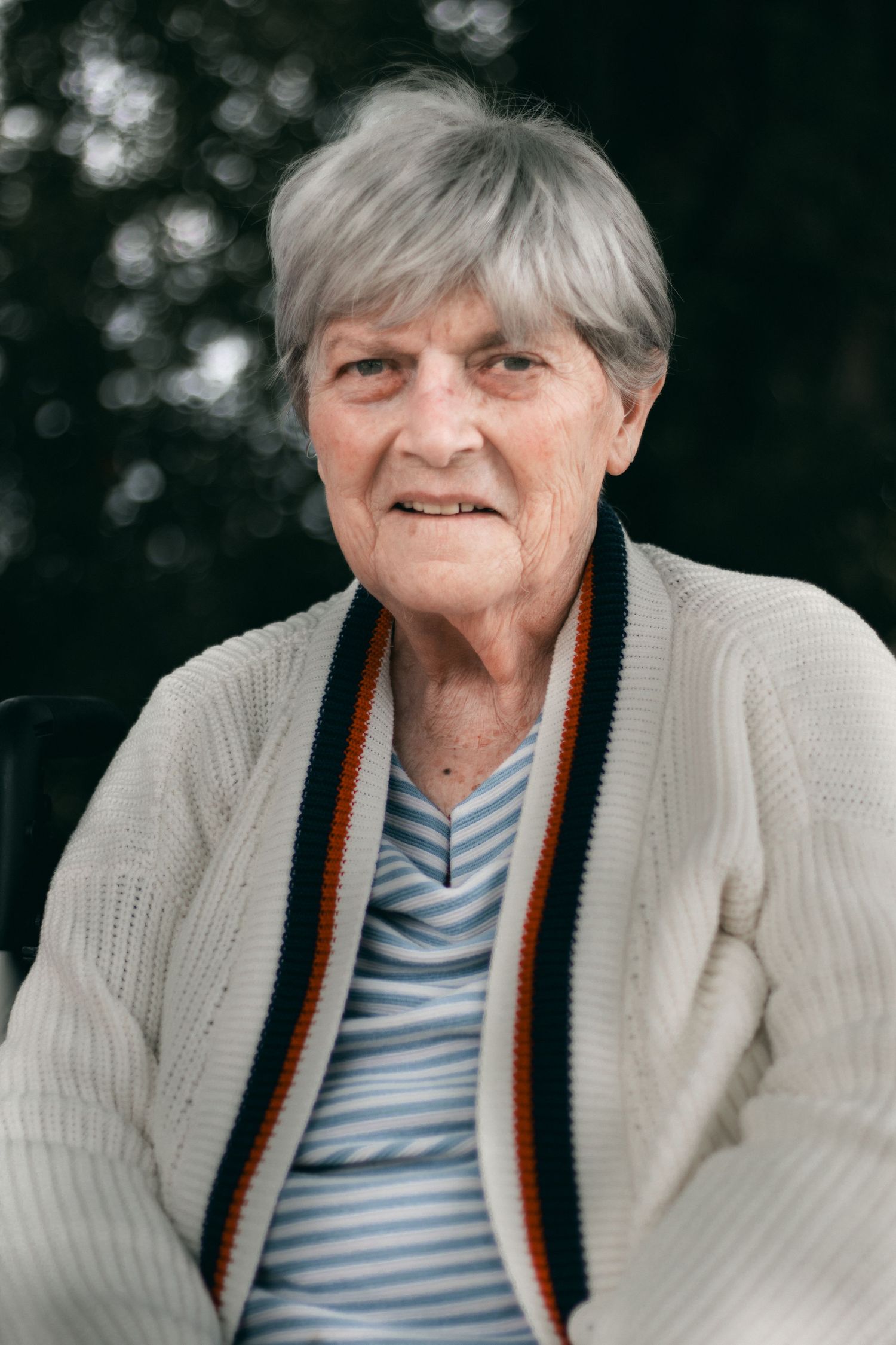 Person in a white cardigan with striped trim and blue striped shirt smiling at the camera.
