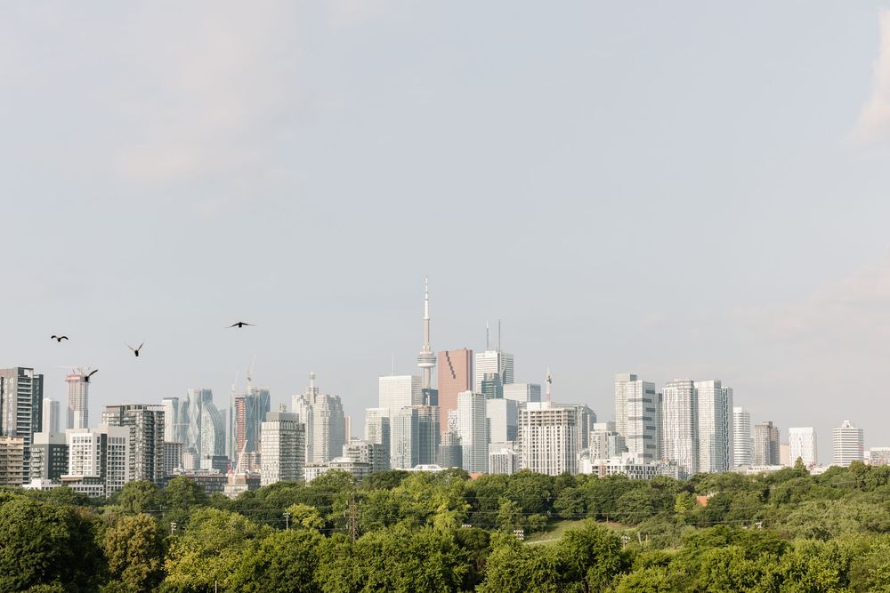 Toronto skyline view with lush green park in foreground against a hazy summer sky.