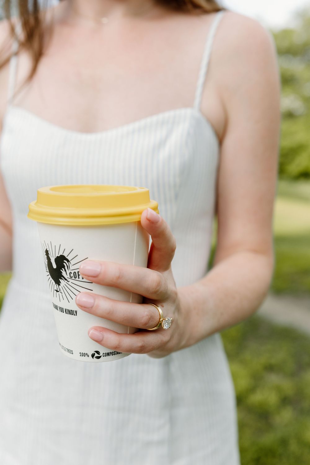 A person in a white dress holds a yellow-lidded coffee cup with an artistic logo design.