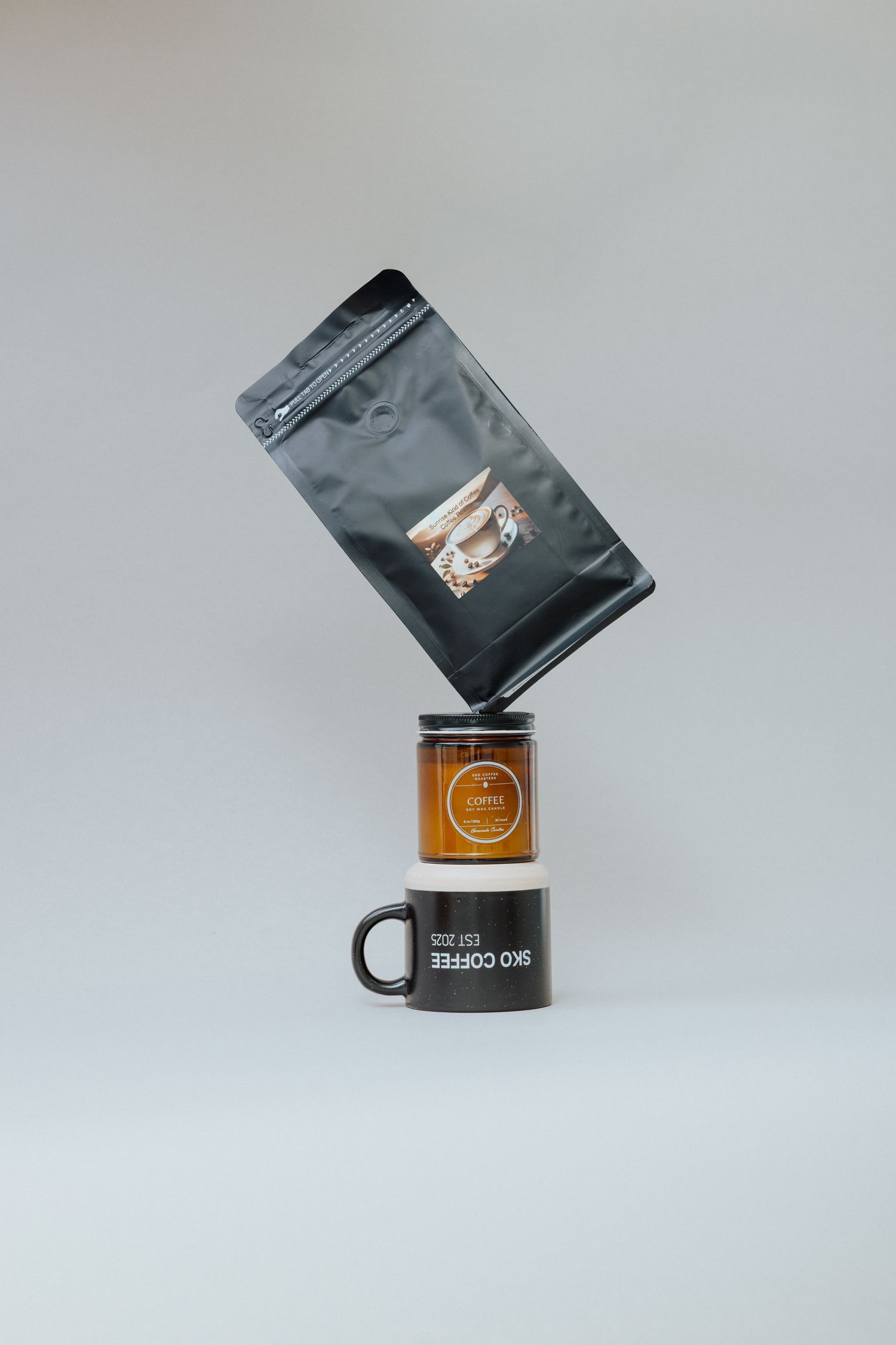 Minimalist studio product shot showing sealed black coffee packets and wood stands in artistic arrangements against gray background.