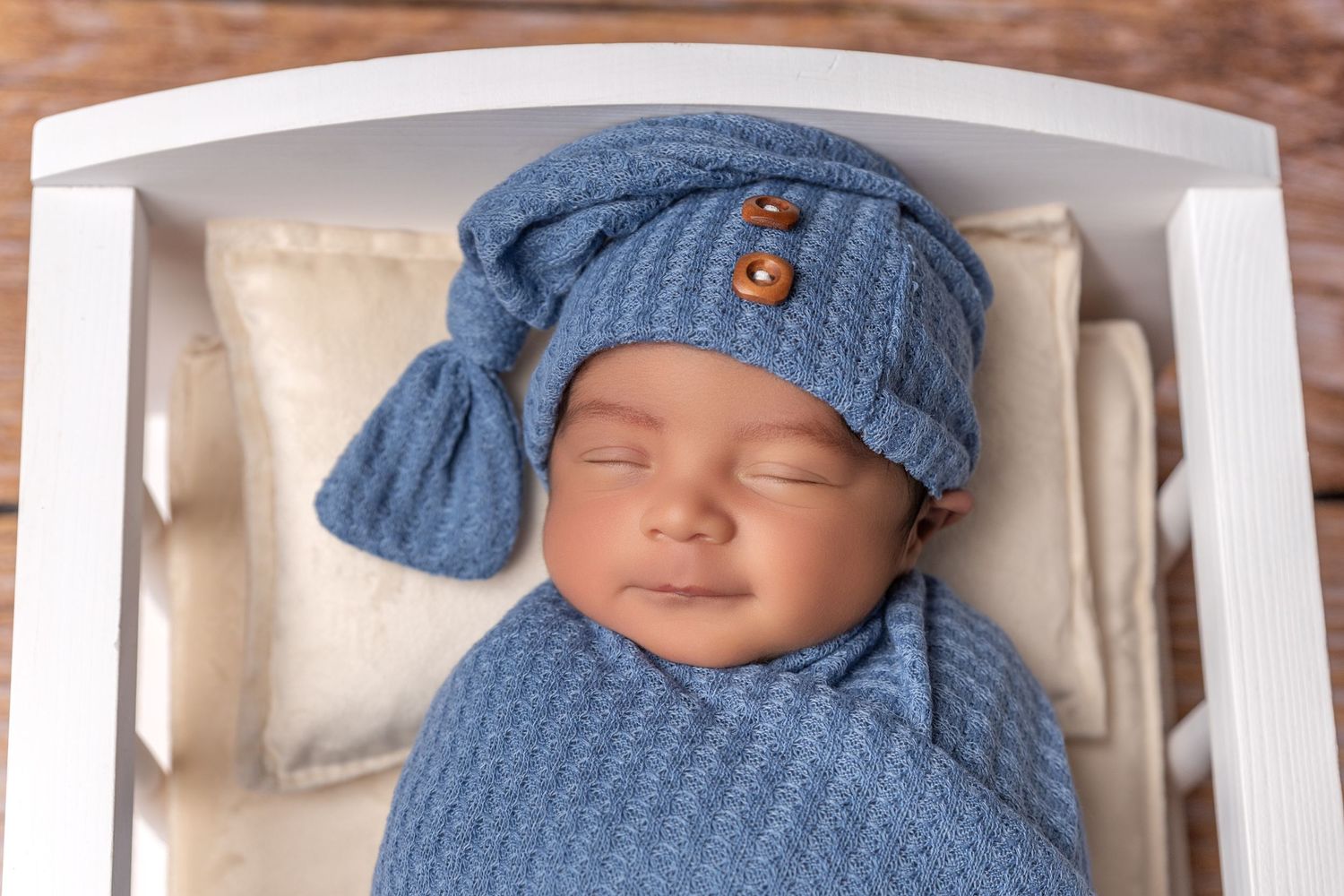Baby girl wearing a white bow headband rests peacefully against white textured bedding in warm natural light.