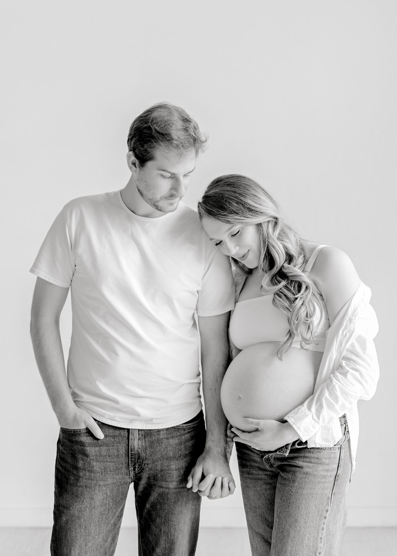 A heartwarming progression of pregnancy photos showing a couple in white shirts and jeans against a plain background.