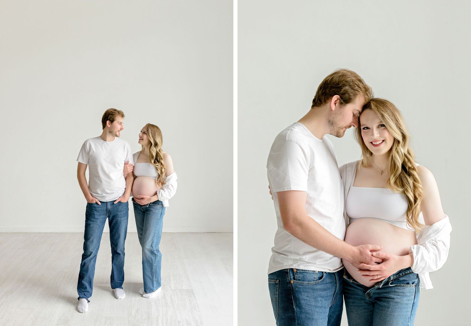 A couple wearing jeans embrace in a minimalist studio setting with white walls and floor.