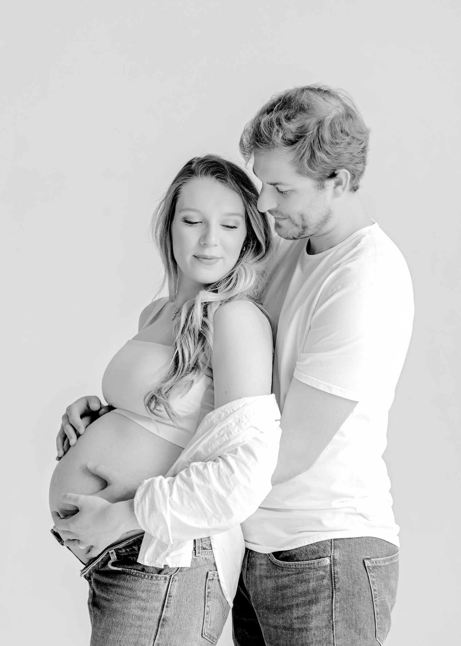 A series of black and white maternity photos showing a couple in tender embrace against a light background.